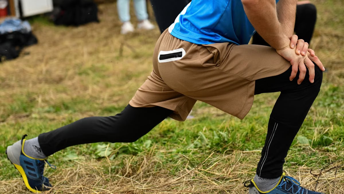 Close-up of a man stretching outdoors in sports attire, focusing on leg muscles and athletic shoes.
